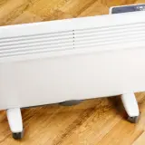 Biały grzejnik elektryczny na kółkach na drewnianej podłodze.