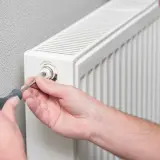 Mężczyzna używa śrubokręta do regulacji zaworu grzejnika aluminiowego. Dowiedz się, jak rozkręcić grzejnik aluminiowy.