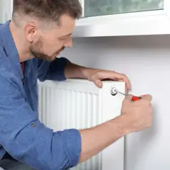 Mężczyzna używa śrubokręta, by prawidłowo odpowietrzyć grzejnik, pozbywając się powietrza z instalacji.