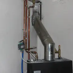 Szara masa uszczelniająca łączy rurę pieca z kominem. Widać też miedziane rurki instalacji grzewczej.