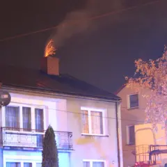 Jasne iskry z komina, czy to normalne? Dym i ogień wydobywają się z ceglanego komina na dachu domu nocą.