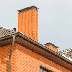 Nowoczesny dom z cegły, z widocznym kominem i dachem. Pomysł na to, jak obudować komin wewnątrz domu, może inspirować się jego zewnętrzną formą.