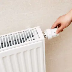 Dłoń reguluje termostat grzejnika. Czy zakręcać grzejniki na noc? To pytanie o oszczędność energii.