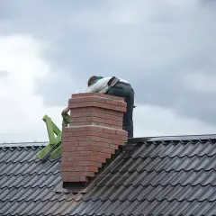 Budowa komina systemowego z cegły na dachu, pracownik w tle.