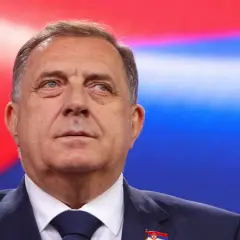 Mężczyzna w garniturze, z flagą Serbii na klapie, na tle czerwono-niebieskim. Czy to symbol kocioł bałkański co to?