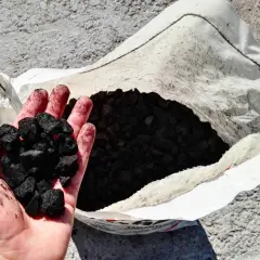 Dłoń trzyma ekogroszek, obok otwarta torba z paliwem. Zastanawiasz się, ile kosztuje ekogroszek w Niemczech?