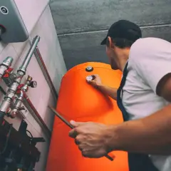 Instalator sprawdza termometr na pomarańczowym bojlerze. Dowiedz się, ile kosztuje piec gazowy do centralnego ogrzewania.
