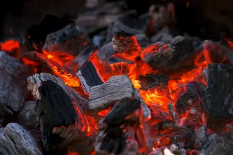 Żarzące się węgle drzewne, które pokazują, jak długo pali się brykiet. Gorące, czerwone żary prześwitują między szarymi i czarnymi kawałkami.
