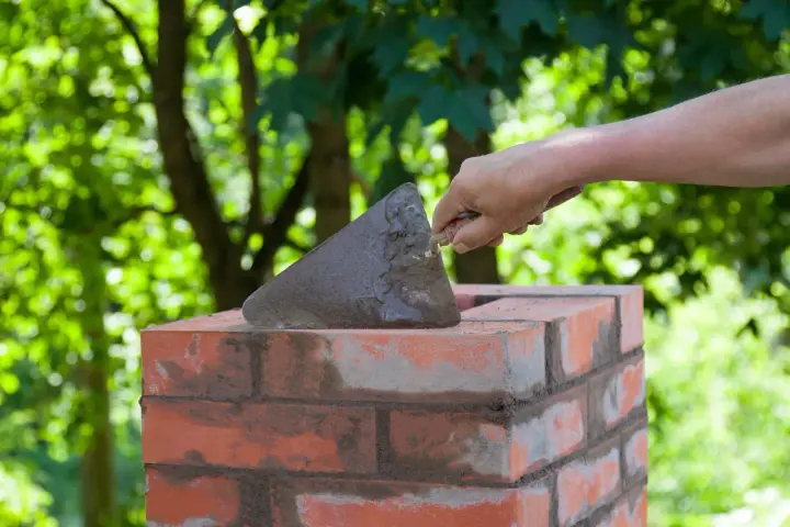 Dłoń z kielnią nakłada zaprawę na cegłę, budując komin. Jaka cegła na komin będzie najlepsza?