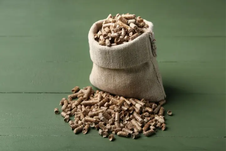 Worek z pelletem drzewnym na zielonym tle. Zastanawiasz się, ile kosztuje worek pelletu?