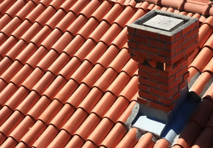Ceglany komin na dachu pokrytym pomarańczową dachówką.