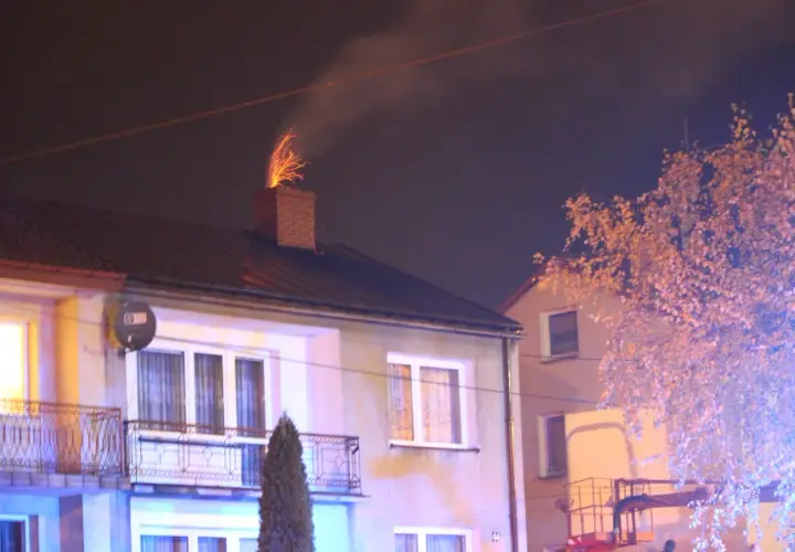 Jasne iskry z komina, czy to normalne? Dym i ogień wydobywają się z ceglanego komina na dachu domu nocą.