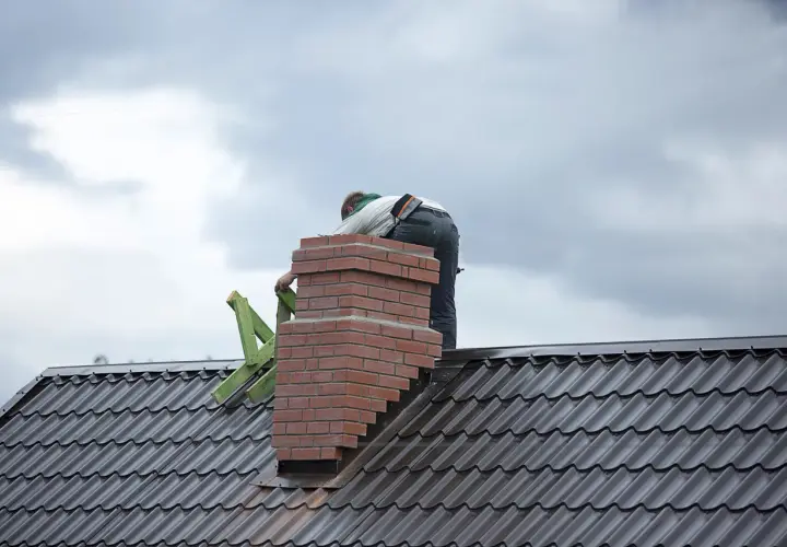 Budowa komina systemowego z cegły na dachu, pracownik w tle.