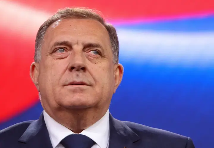 Mężczyzna w garniturze, z flagą Serbii na klapie, na tle czerwono-niebieskim. Czy to symbol kocioł bałkański co to?