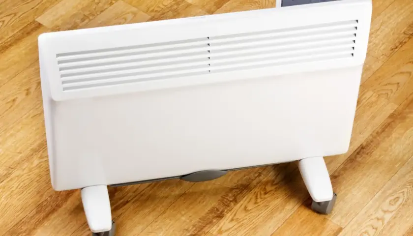 Biały grzejnik elektryczny na kółkach na drewnianej podłodze.