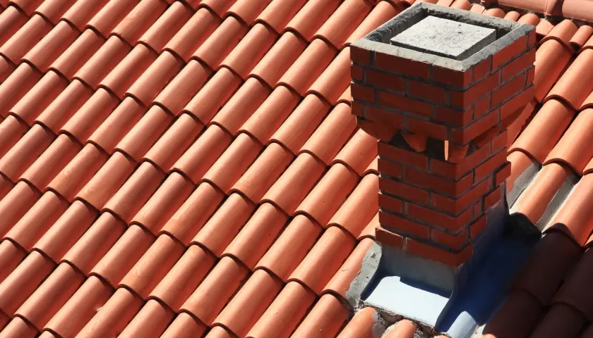 Ceglany komin na dachu pokrytym pomarańczową dachówką.