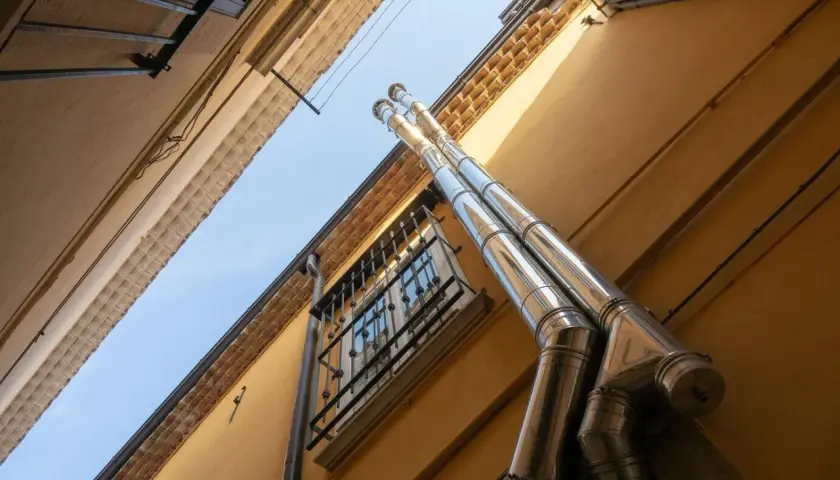 Dwa błyszczące kominy wychodzą z żółtej ściany. Zastanawiasz się, jak zmniejszyć ciąg w kominie?