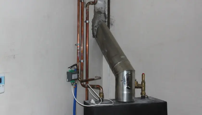 Szara masa uszczelniająca łączy rurę pieca z kominem. Widać też miedziane rurki instalacji grzewczej.