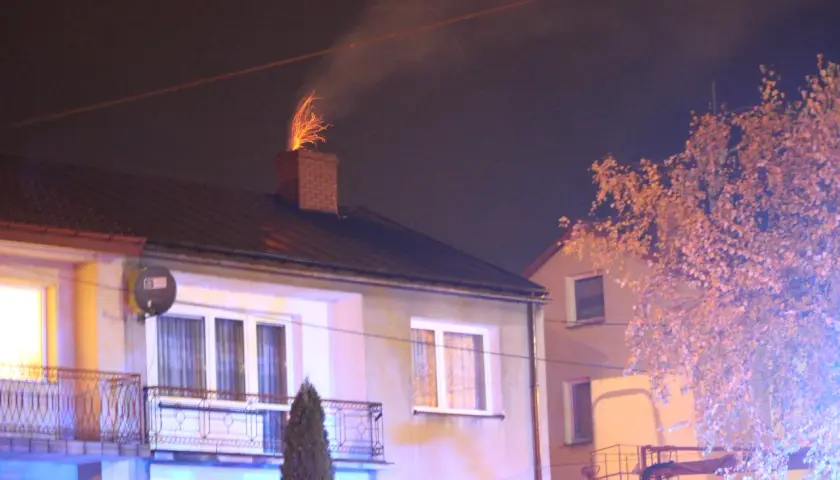 Jasne iskry z komina, czy to normalne? Dym i ogień wydobywają się z ceglanego komina na dachu domu nocą.