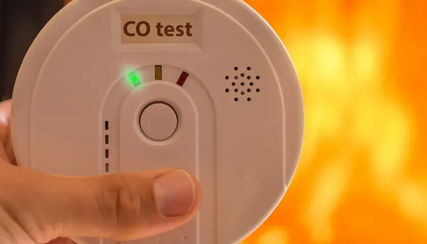 Biały czujnik czadu z zieloną diodą i napisem "CO test" w dłoni. Sprawdź, jak działa czujnik czadu, by zapewnić bezpieczeństwo.