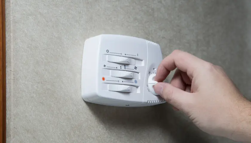 Dłoń kręci pokrętłem termostatu. Ustawienie temperatury wpływa na pracę kotła, a jego histereza decyduje o częstotliwości włączania i wyłączania.