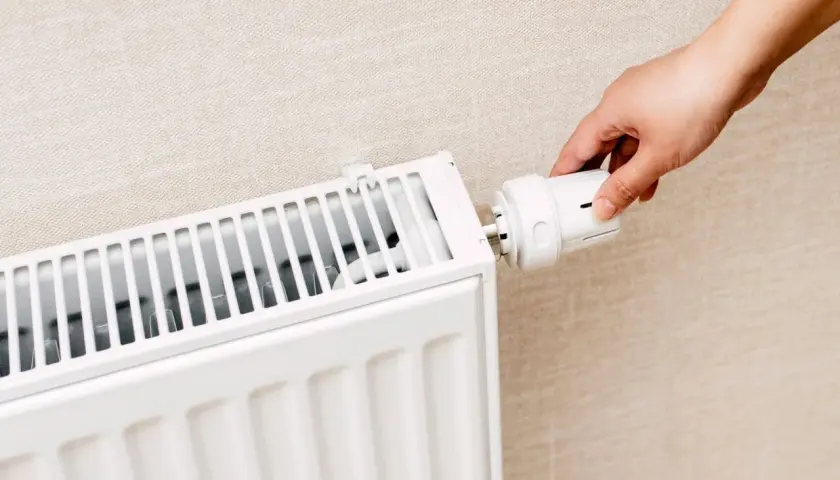 Dłoń reguluje termostat grzejnika. Czy zakręcać grzejniki na noc? To pytanie o oszczędność energii.