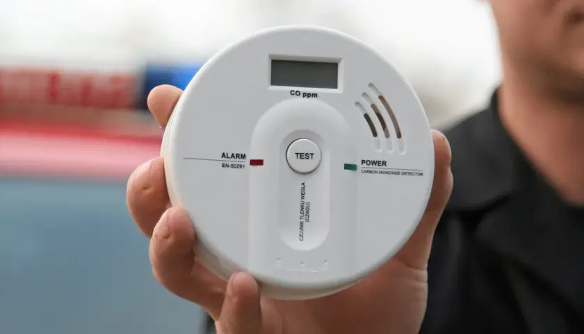 Biały czujnik czadu trzymany w dłoni, z wyświetlaczem CO ppm i przyciskiem TEST.