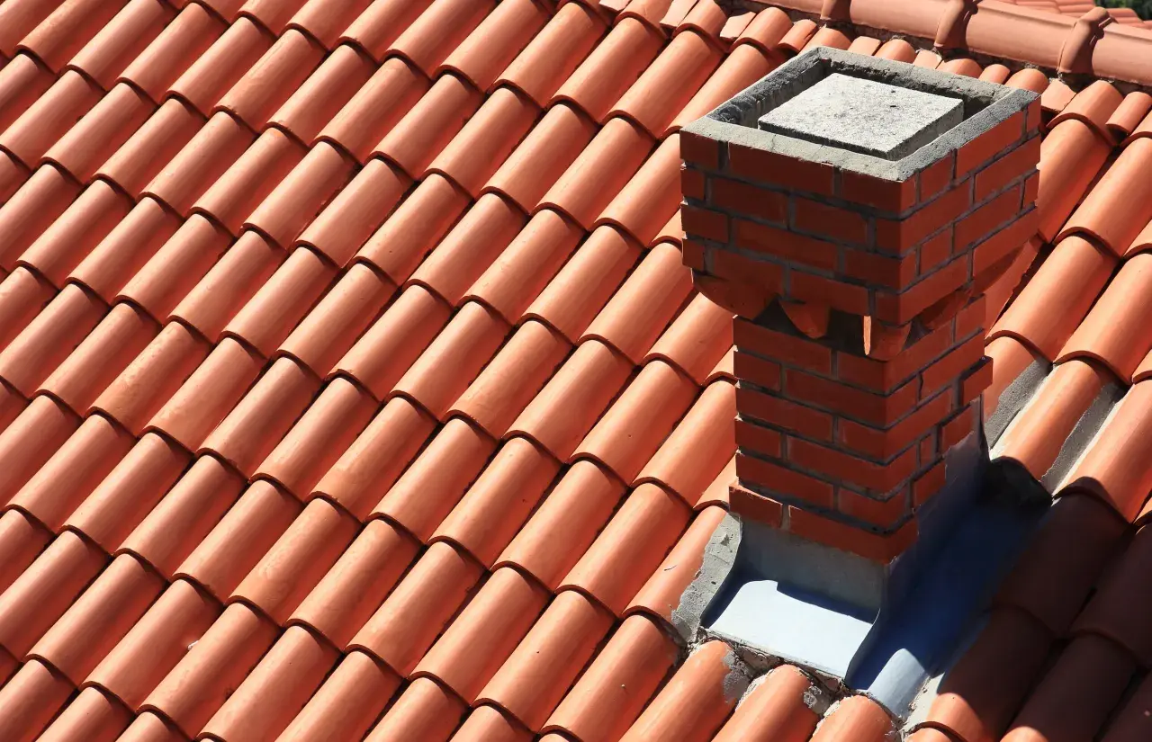 Ceglany komin na dachu pokrytym pomarańczową dachówką.