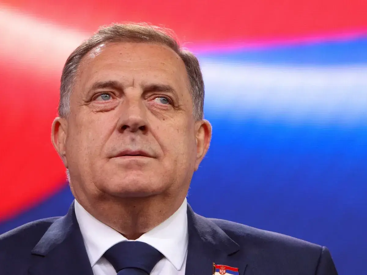Mężczyzna w garniturze, z flagą Serbii na klapie, na tle czerwono-niebieskim. Czy to symbol kocioł bałkański co to?