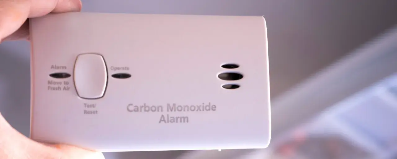 Biały czujnik czadu z przyciskiem Test/Reset i napisami "Alarm", "Move to Fresh Air", "Operate", "Carbon Monoxide Alarm".