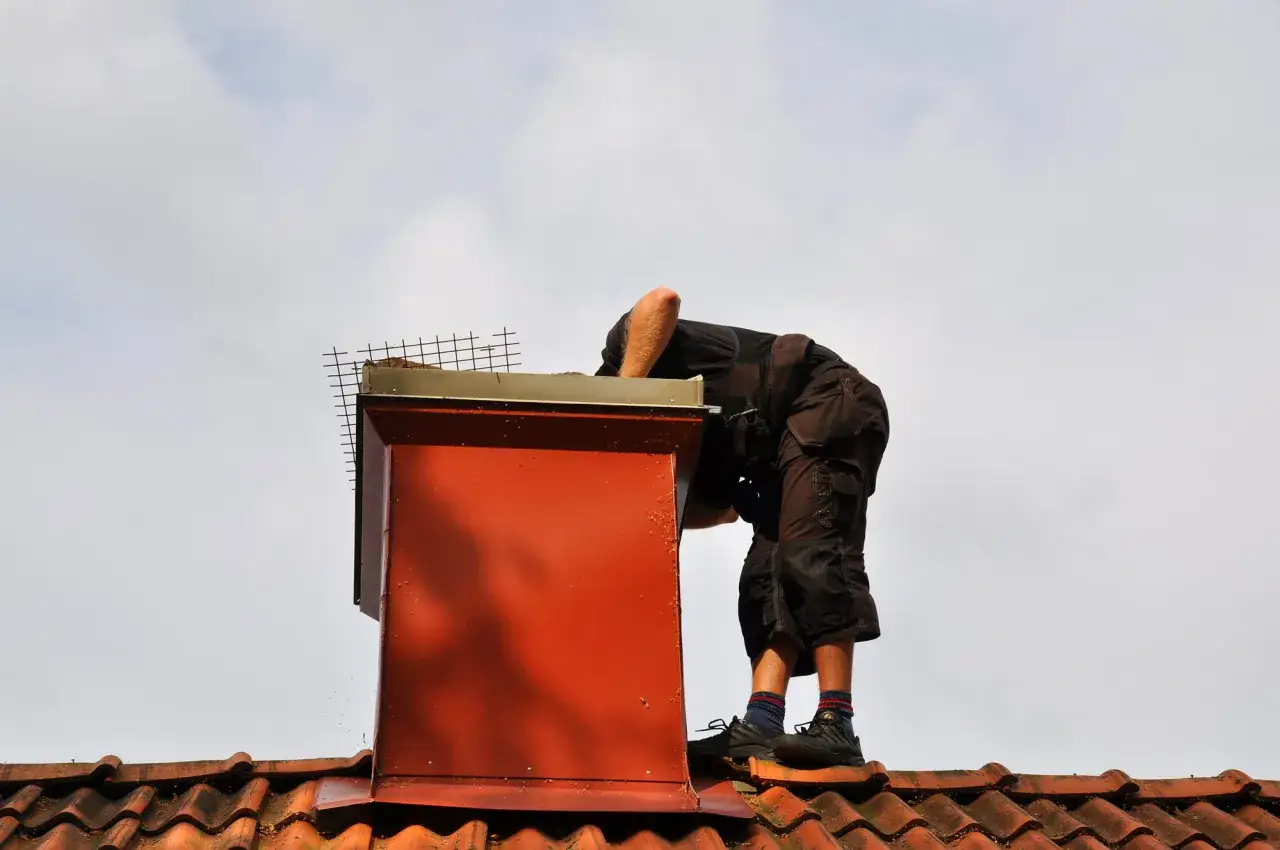 Pracownik sprawdza dach i komin, szukając objawów nieszczelności.