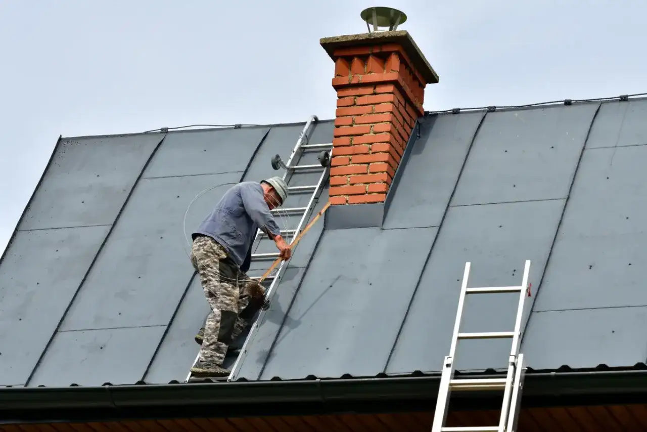 Kominiarz na drabinie czyści ceglany komin. Zastanawiasz się, ile kosztuje czyszczenie komina?
