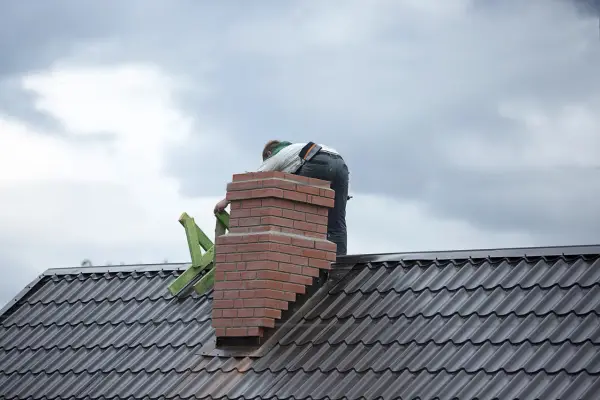 Budowa komina systemowego z cegły na dachu, pracownik w tle.